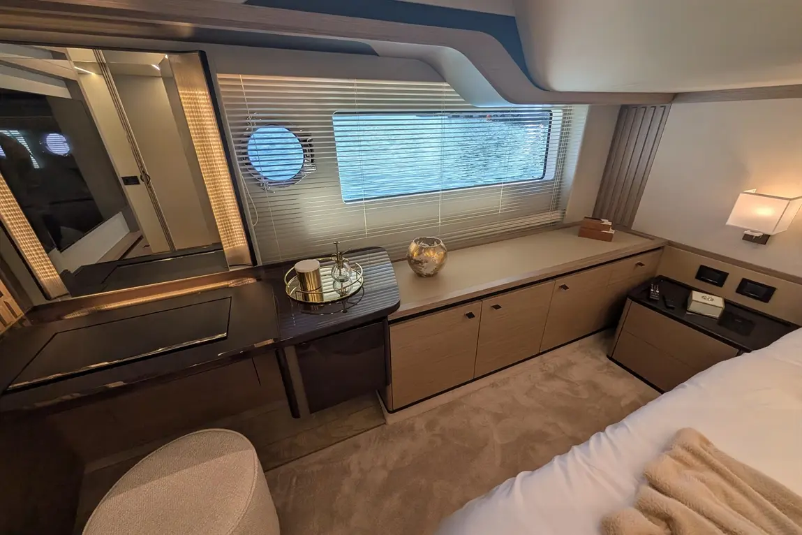 Modern yacht cabin interior with a round window, stylish desk, decorative vase, and neutral colour scheme.